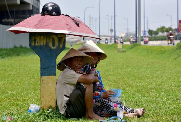 Tại khu vực gần cầu vượt Cát Lái (quận 2), vợ chồng ông Trần Văn Nông (quận 2), cùng ngồi bên cột km, che nắng bằng chiếc dù nhỏ giữa bãi cỏ đợi khách mua những chiếc khăn đa năng.